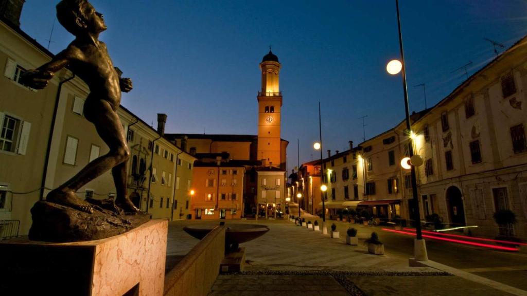 uma estátua de um homem numa rua com uma torre de relógio em Cormons Bellissima em Cormòns