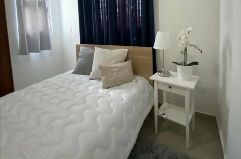 a bedroom with a white bed with a white night stand at Reposo Tranquilidad cerca del corazón de Santiago in Santiago de los Caballeros
