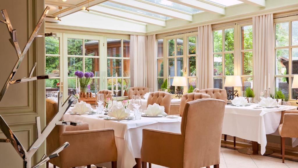 a dining room with white tables and chairs and windows at Superior Hotel Tirolerhof - Zell am See in Zell am See