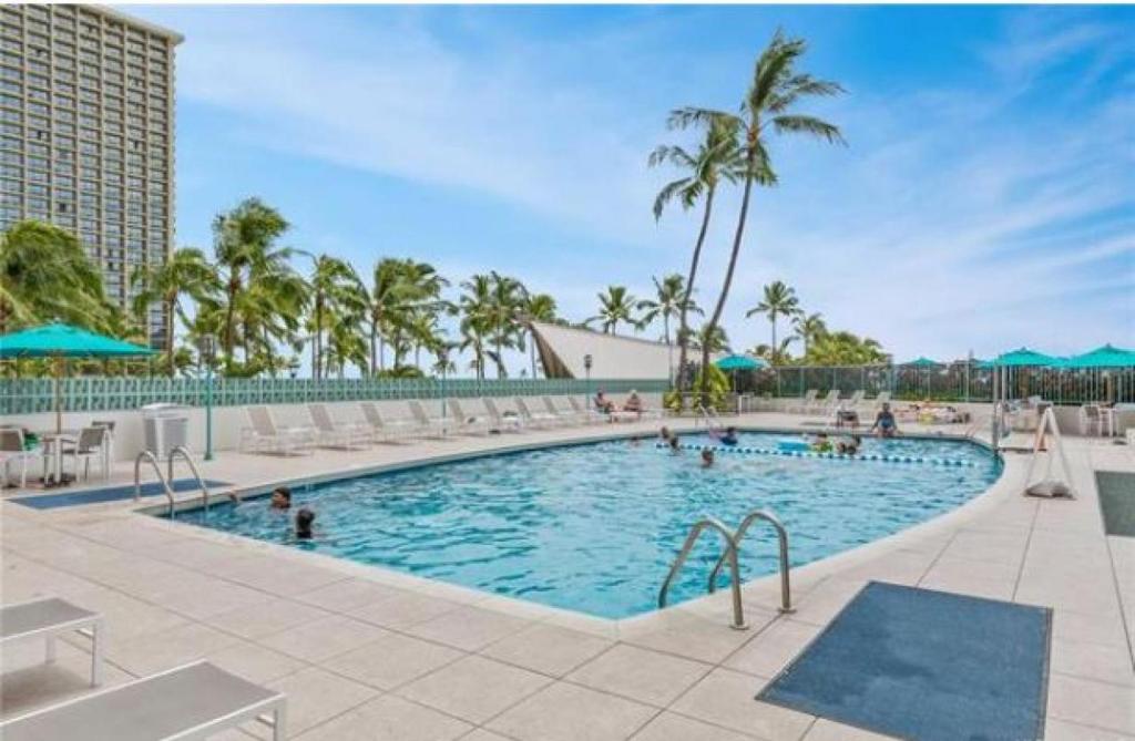a large swimming pool with chairs and palm trees at Ilikai Tower 633 Yacht Harbor View 1BR in Honolulu
