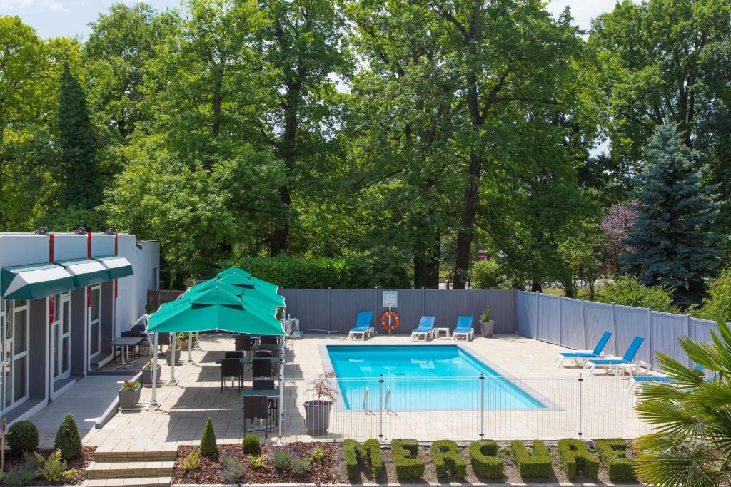 a pool with chairs and umbrellas in a yard at Mercure Strasbourg Aéroport in Ostwald