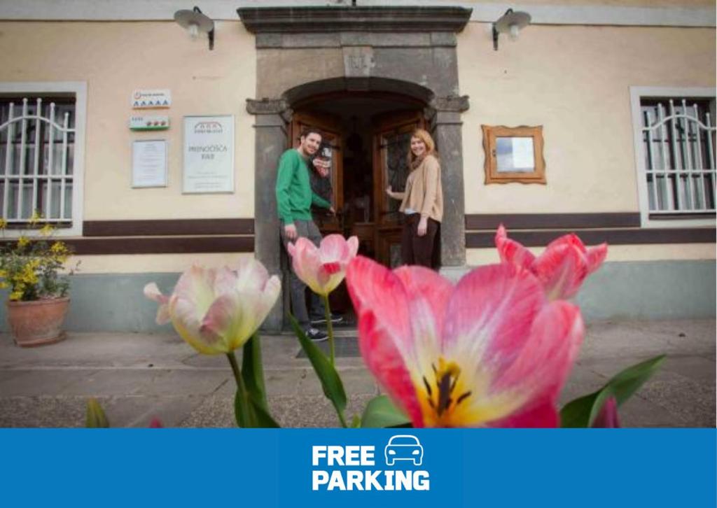 a man and woman standing outside a building with pink flowers at B&B Pod Skalo in Kamnik