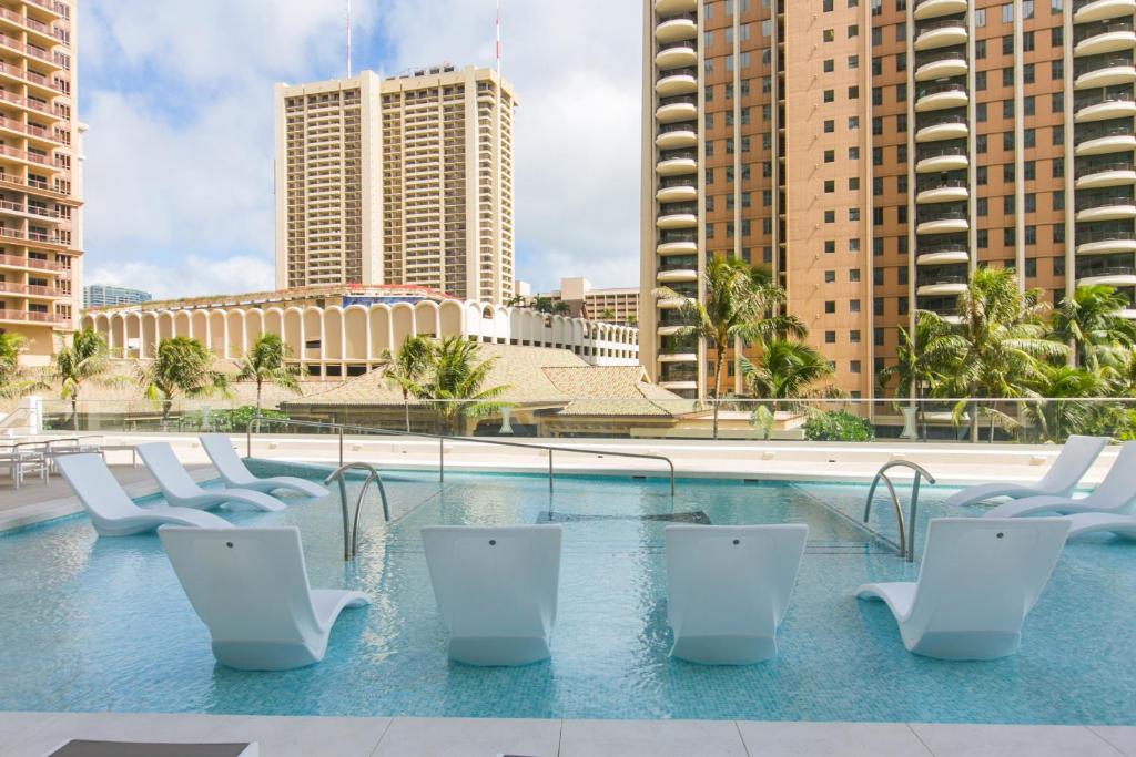 a swimming pool with white chairs and tall buildings at Ilikai Tower 1915 City View 1BR in Honolulu