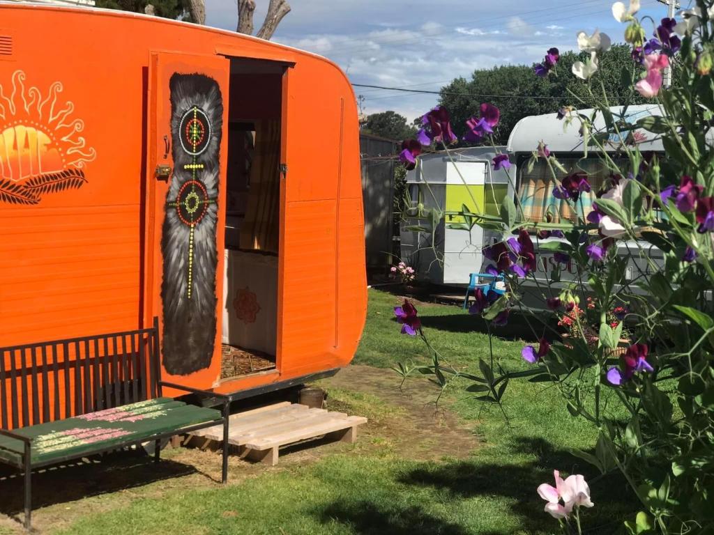 einen orangenen Wohnwagen in einem Hof mit einer Bank und Blumen in der Unterkunft Morepork Rural Oasis in Aongatete