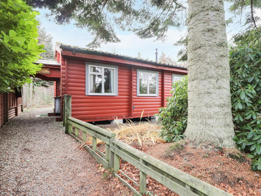 uma cabana vermelha com uma cerca ao lado de uma árvore em Rowan Lodge em Strathpeffer