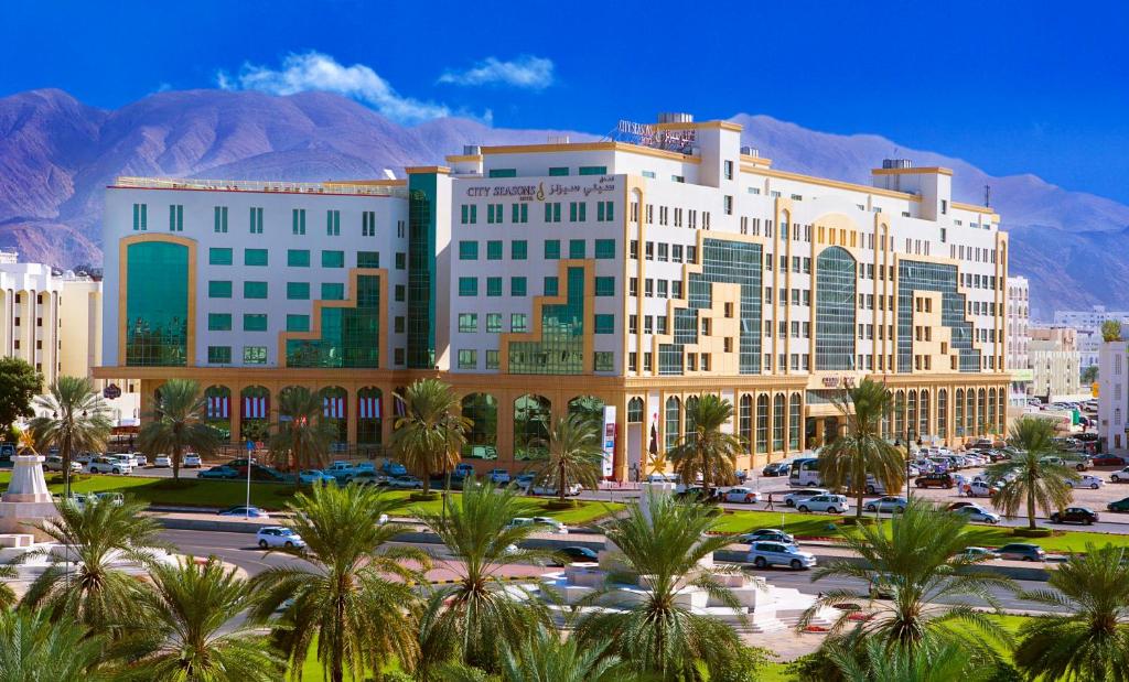 City Seasons Hotel & Suites Muscat في مسقط: مبنى كبير فيه نخل في موقف للسيارات