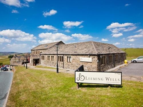 una señal frente a un edificio de piedra con una señal en Leeming Wells, en Haworth