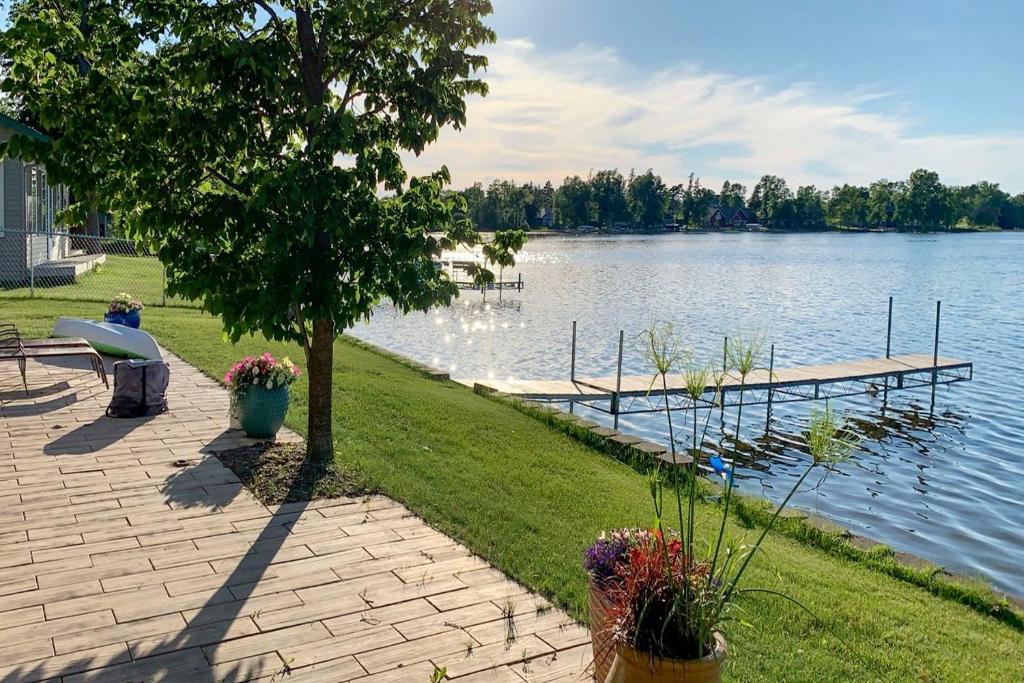 a lake with a pier and a bench and flowers at The Lakefront Home - 5 Minutes From Detroit Lakes! in Detroit Lakes