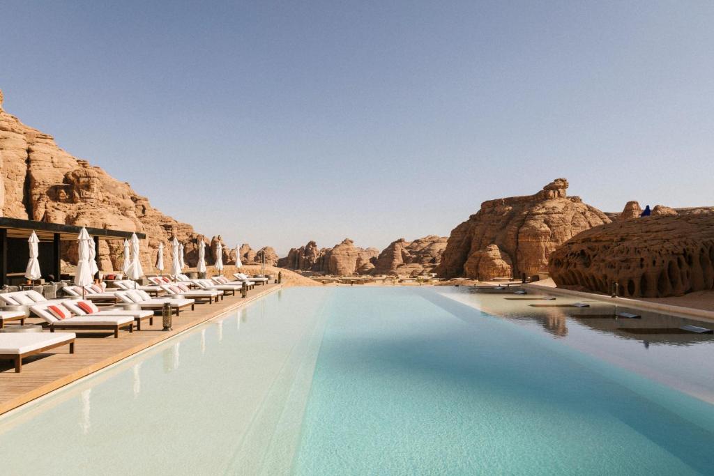 une piscine dans le désert avec des chaises et des rochers dans l'établissement Our Habitas AlUla, à Al-Ula