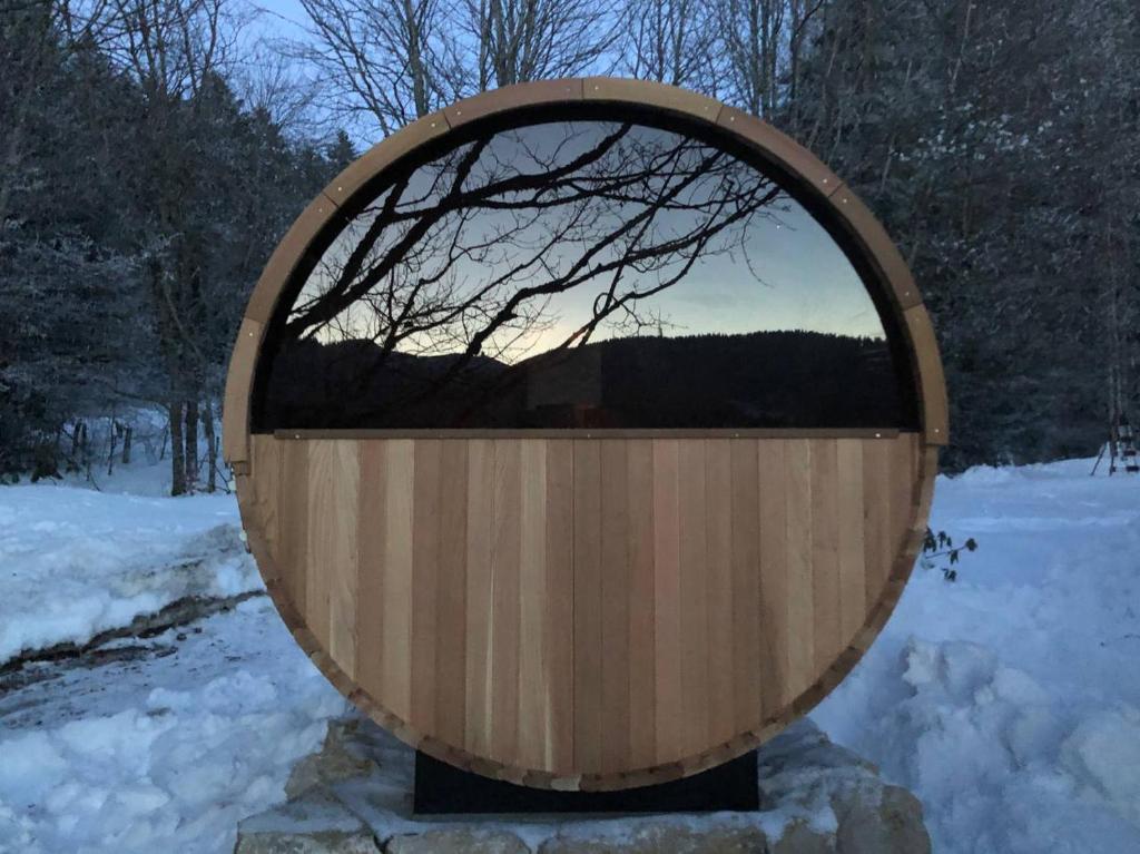 uma banheira de madeira redonda com uma janela na neve em Chalet OTT - apartment in the mountains with sauna em Saint-Cergue