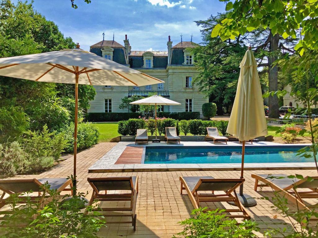 a pool with chairs and umbrellas in front of a house at La Seignère in Saumur