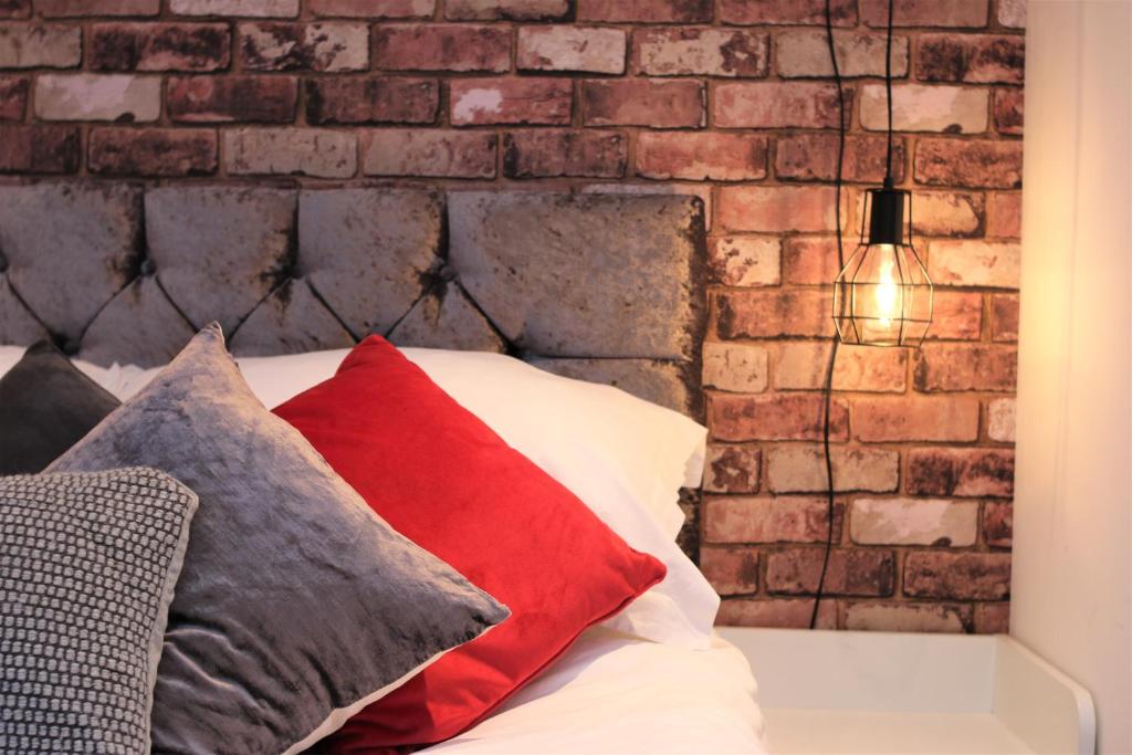 a brick wall behind a bed with red pillows at Northcote Lane Apartments by Property Promise in Cardiff