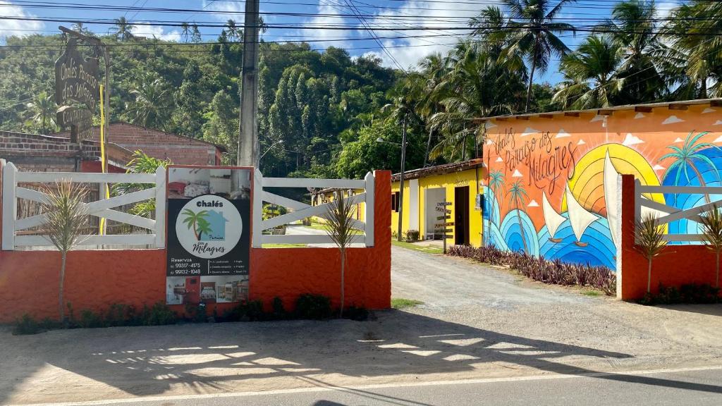 een hek met een muurschildering aan de zijkant van een gebouw bij Chalés Paraíso dos Milagres in São Miguel dos Milagres