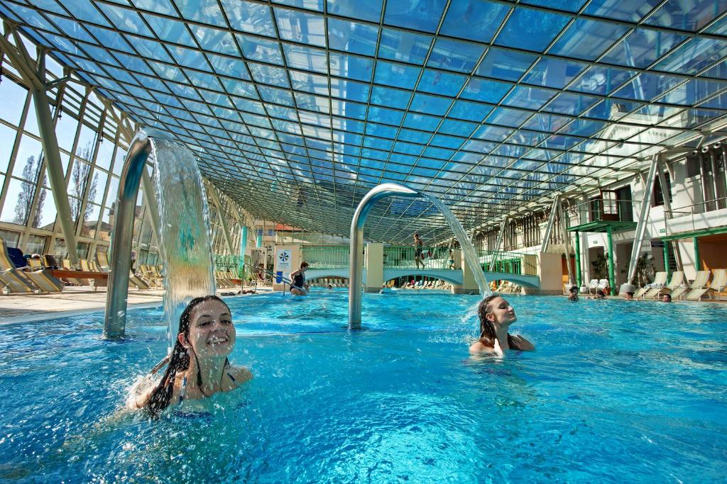 two women swimming in a swimming pool with a roof at Das Gutenbrunn Thermen & Sporthotel in Baden