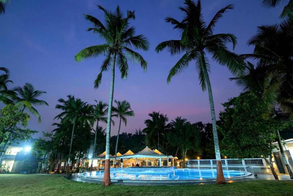 un complejo con piscina y palmeras por la noche en Gold Beach Villa, en Daman