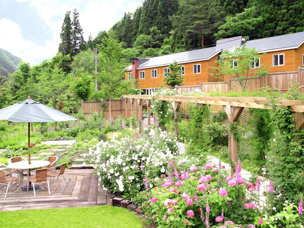 een tuin met bloemen en een tafel en een parasol bij Pension Asanebou in Minakami