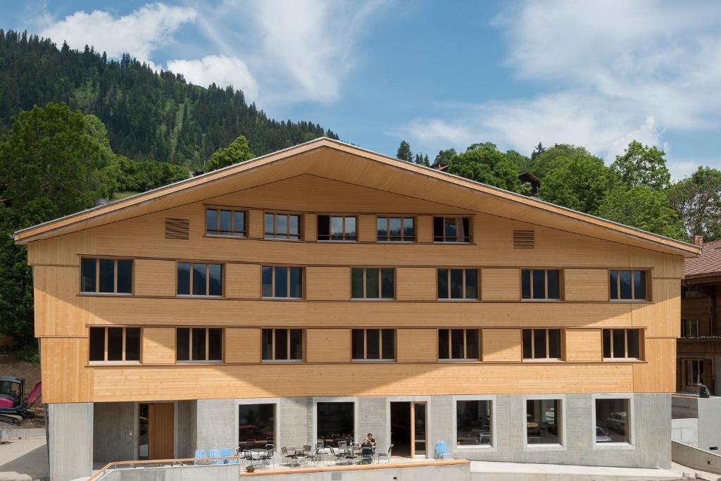 ein großes Holzgebäude mit Fenstern vor einem Berg in der Unterkunft Gstaad Saanenland Youth Hostel in Gstaad