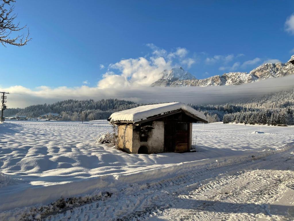 a small building in a snow covered field with mountains at Appartement Oberlacken in Sankt Johann in Tirol