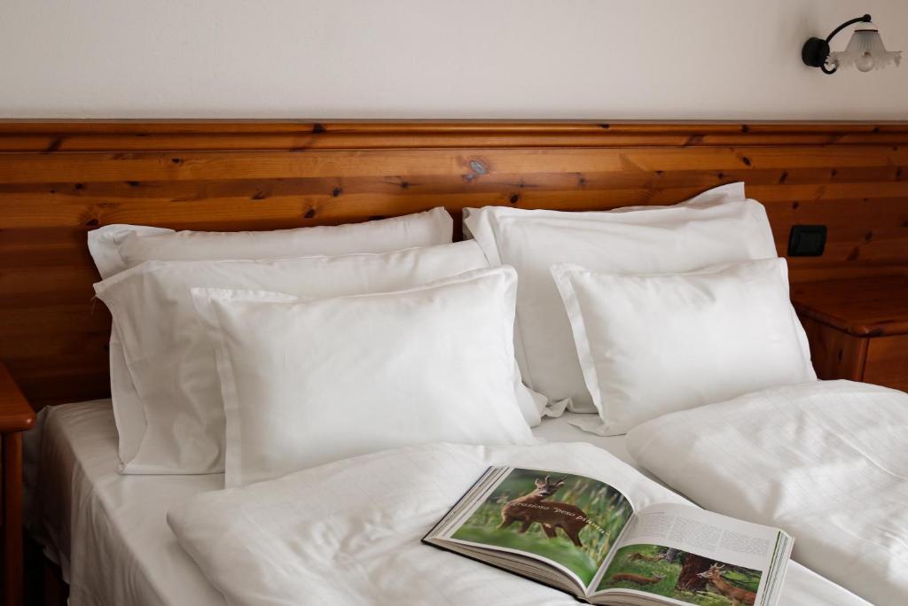 a bed with white pillows and a book on it at Hotel Garni Civetta in Selva di Cadore