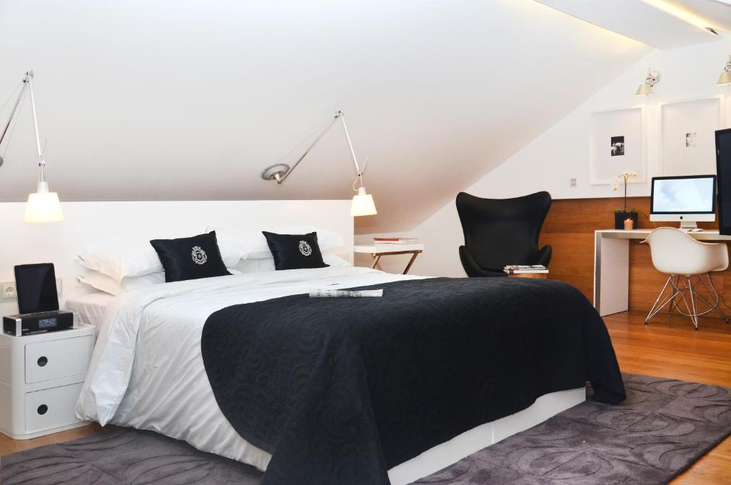 An attic-style bedroom with a black-and-white bed, lounge chair and desk beneath a sloped ceiling.