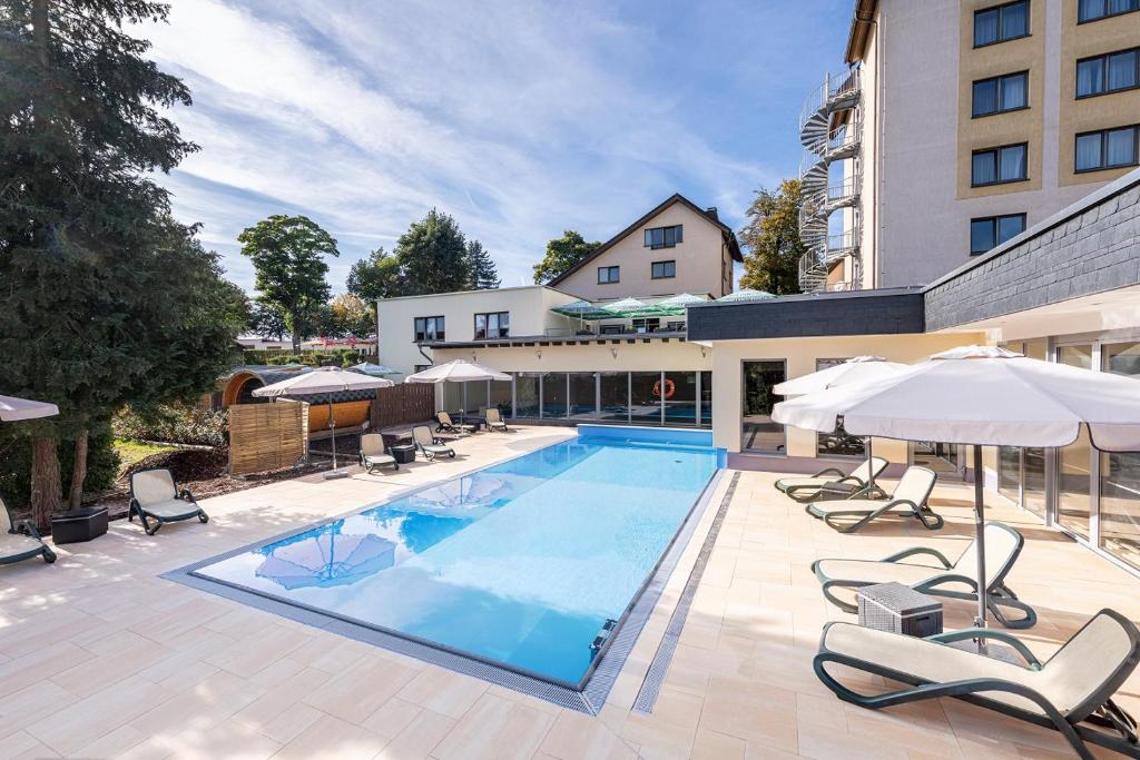 einen Pool mit Stühlen und Sonnenschirmen neben einem Gebäude in der Unterkunft Akzent Aktiv & Vital Hotel Thüringen in Schmalkalden