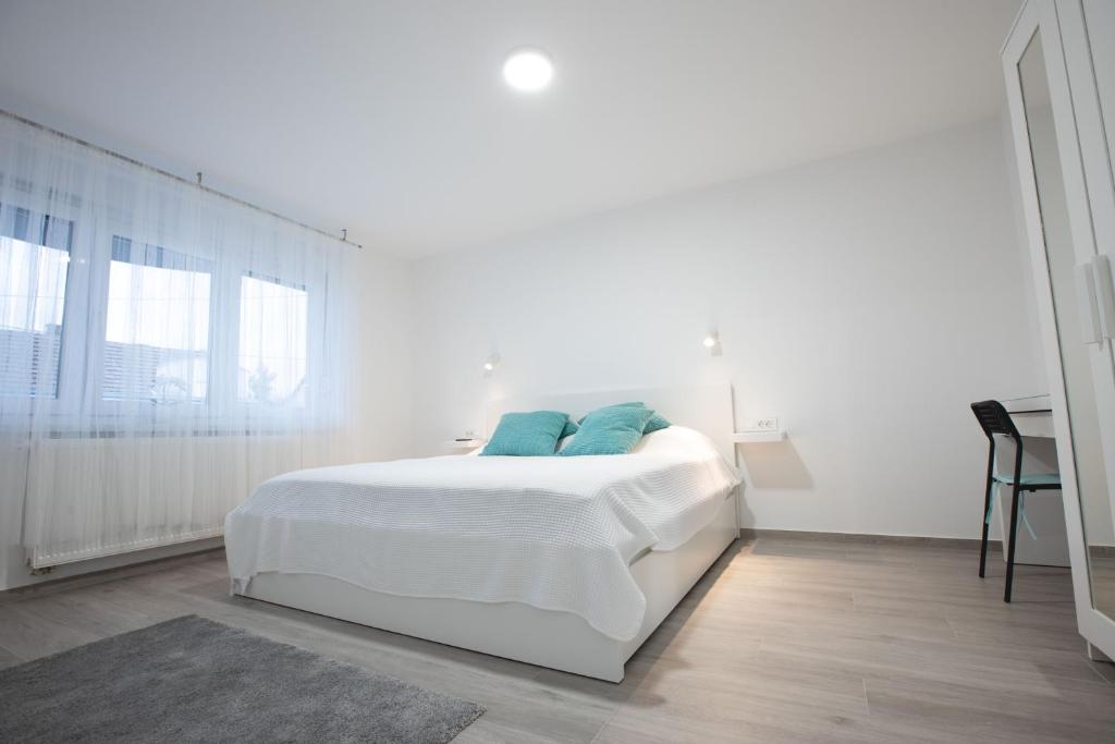 a white bedroom with a white bed with blue pillows at Apartmani Dora in Požega