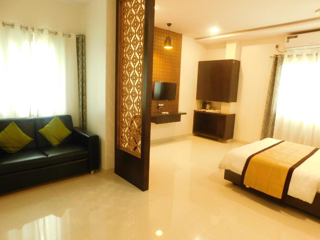 a bedroom with a bed and a couch and a television at Hotel Neem Tree in Shirdi