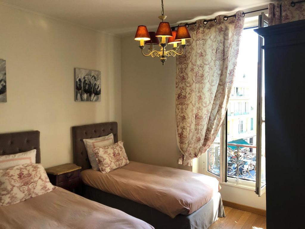 a bedroom with two beds and a window with a chandelier at Hotel La Regence in Villefranche-sur-Mer