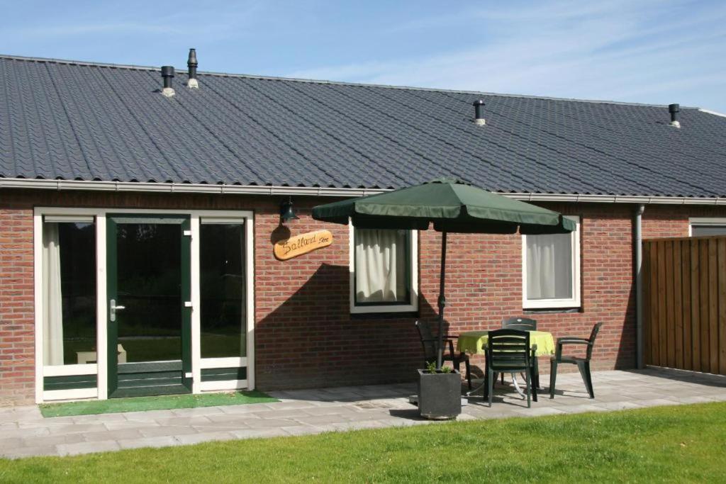 uma casa de tijolos com um pátio com um guarda-chuva verde em De Huttert- Salland Stee em Luttenberg