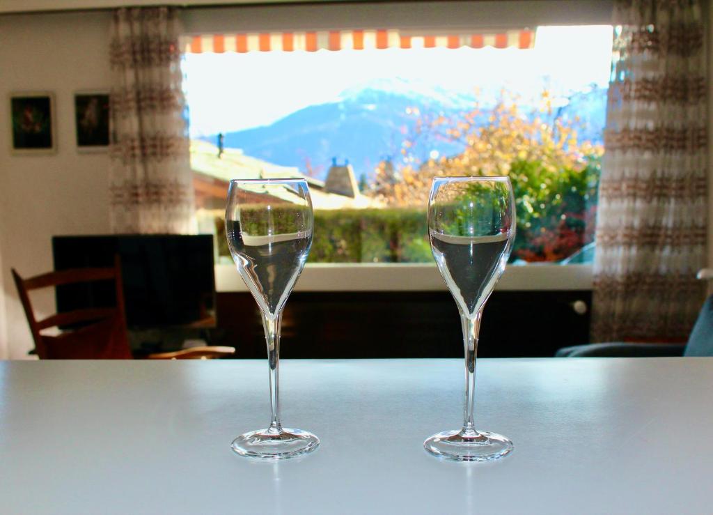 two wine glasses sitting on a table in front of a window at Hautes Roches - Magnifique vue sur la montagne in Crans-Montana