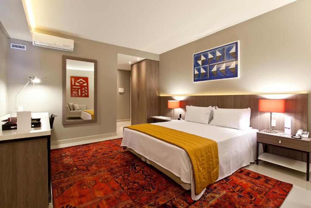 Pokój hotelowy z dużym łóżkiem i biurkiem w obiekcie San Diego Suites Veredas Sete Lagoas w mieście Sete Lagoas