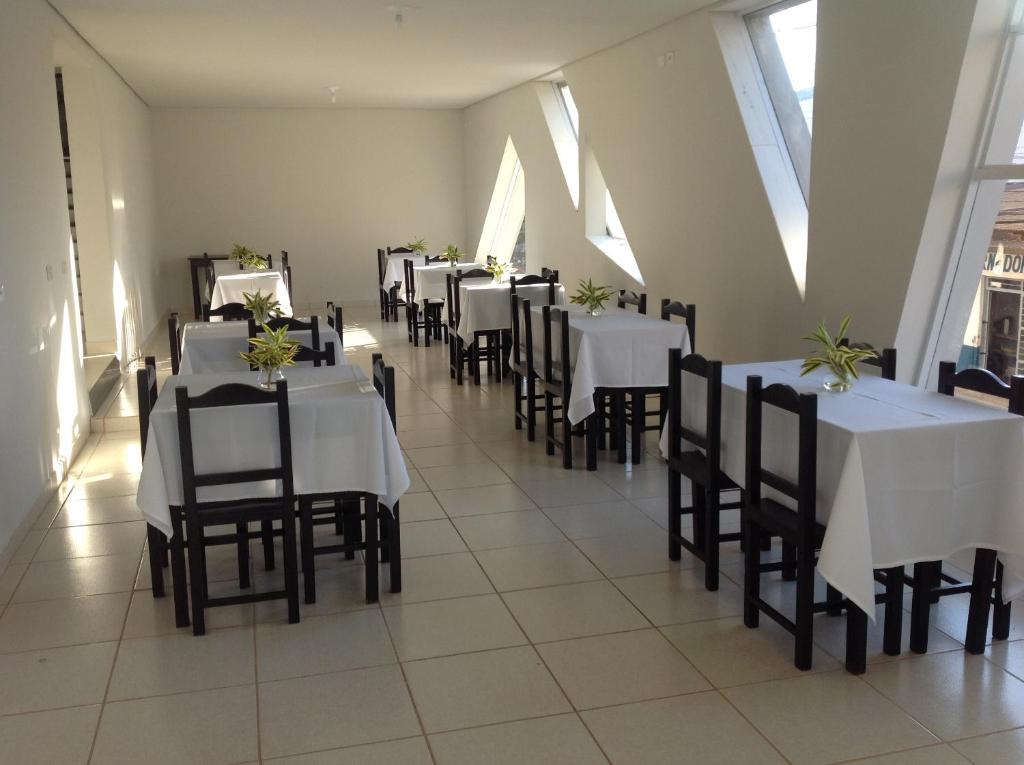 Itumbiara Palace Hotel في إيتومبيارا: غرفة طعام مع طاولات بيضاء وكراسي سوداء