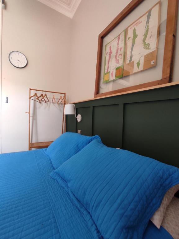 a bedroom with a bed with blue sheets and a clock at Hostal Dinamarca in Valparaíso