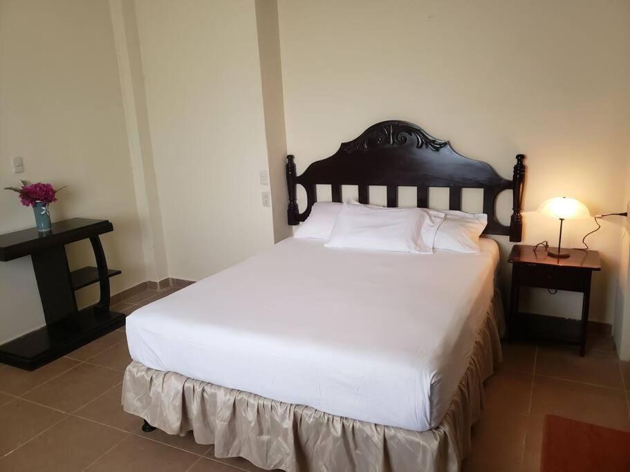 a bedroom with a large white bed with a wooden headboard at Casa de campo by the river in Estelí