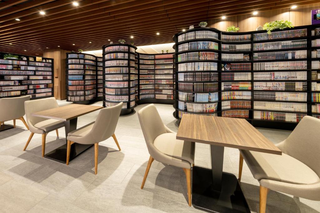 a library with two tables and chairs and stacks of books at TheHedistarHotel KyotoNijo Comic&Books in Kyoto