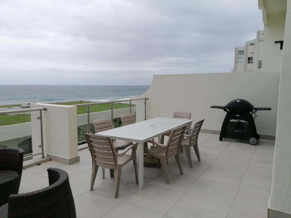 307 Bermudas - by Stay in Umhlanga في ديربان: طاولة وكراسي على شرفة مع المحيط