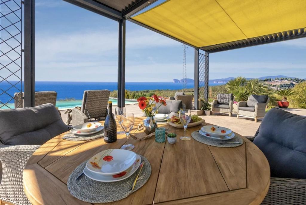 Villa Luxury Sunshine Alghero con piscina vista mare في ألغيرو: طاولة طعام خشبية مطلة على المحيط