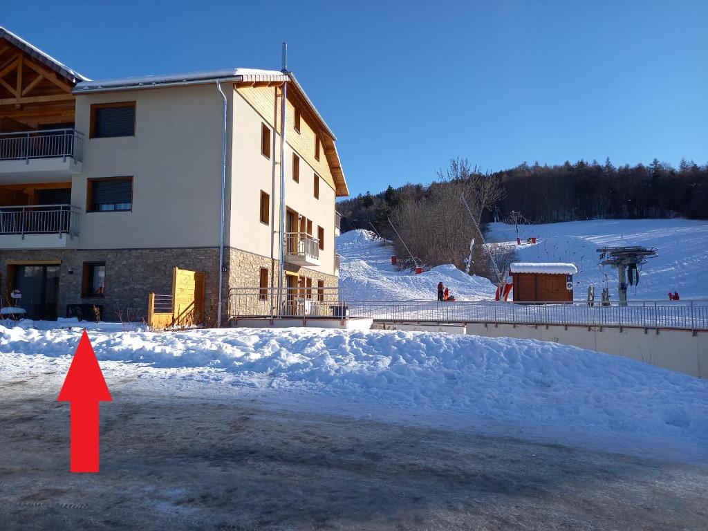 Una flecha roja apunta a un edificio en la nieve en Appartement Les Vallons au pied des pistes, en Ancelle