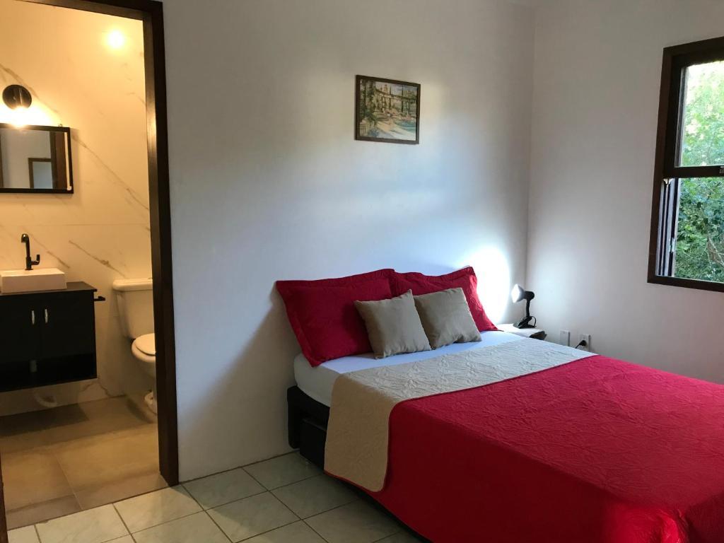 1 dormitorio con cama roja y baño en Apartamento do Norte na Ferrugem, en Garopaba