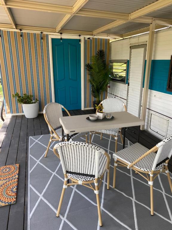 un patio con mesa y sillas en un porche en Crescent Head, stylish retro caravan, deck, bathroom, private bush setting near beach, en Crescent Head