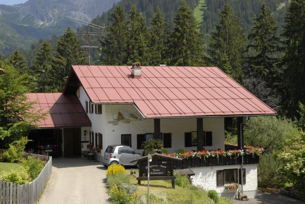 ein Haus mit rotem Dach mit einem Auto in der Einfahrt in der Unterkunft Bergführer-Hüsle in Mittelberg