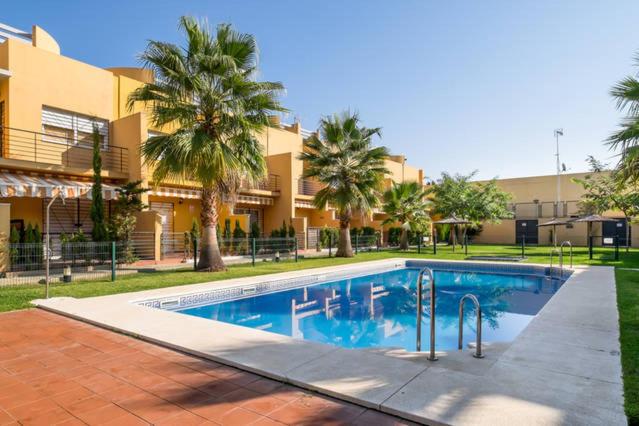 a swimming pool in front of a building with palm trees at Dorado Playa in Huelva