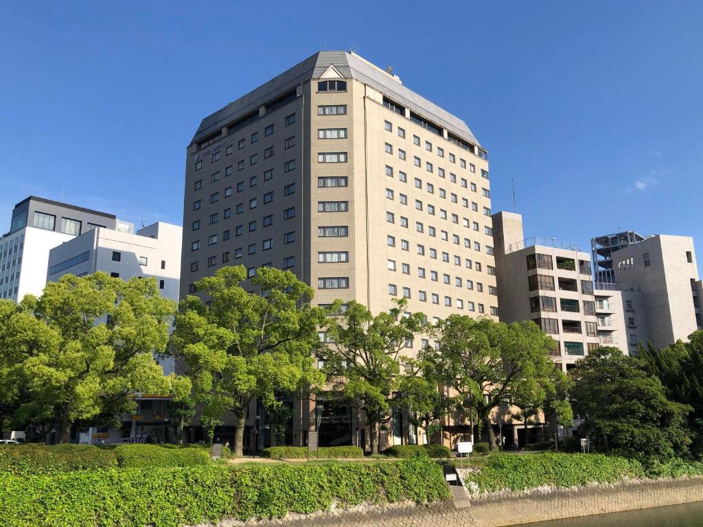 um edifício alto e branco com árvores em frente em HOTEL MYSTAYS Hiroshima Peace Park em Hiroshima