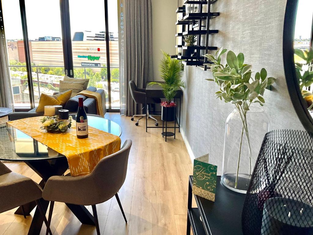 een eetkamer met een tafel en stoelen en een kamer met ramen bij 5 Star Elegant Apartments, Ellipse Waterfall City, Midrand, Johannesburg in Midrand