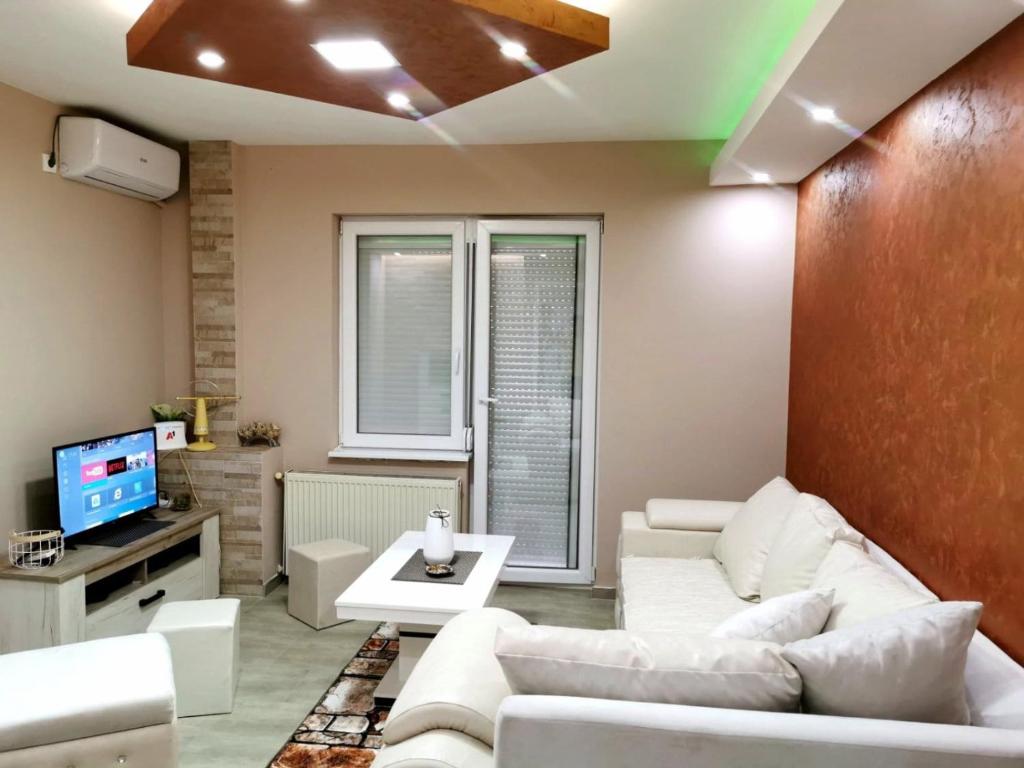 sala de estar con sofás blancos y TV en Lux Apartman Krstic, en Kruševac