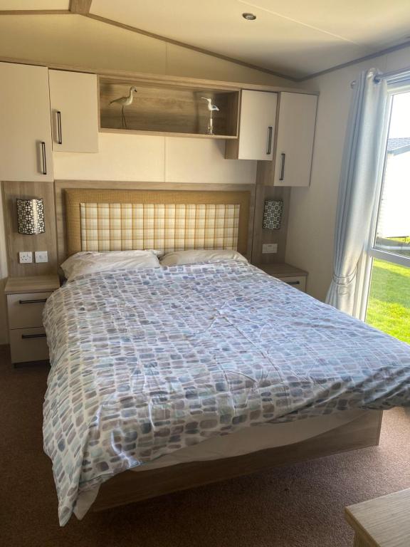 a bedroom with a bed with a blue and white comforter at holidayhome-romneysands holiday park in Littlestone-on-Sea