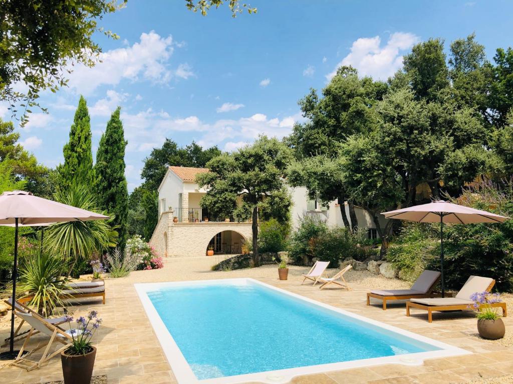 uma piscina com cadeiras e guarda-sóis ao lado de uma casa em Maison Les Costes em Vernègues