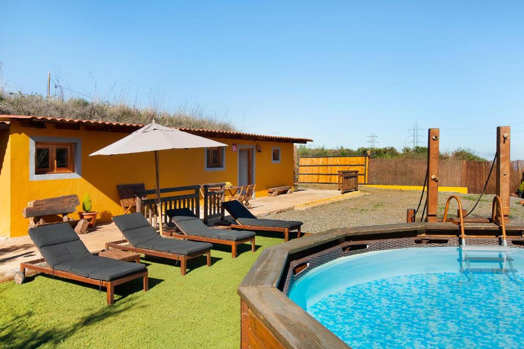 een zwembad met stoelen en een parasol naast een huis bij Casa Rural Los Colorados in Vega de San Mateo