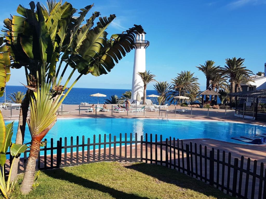 un palmier à côté d'une piscine avec un phare dans l'établissement Atlantic Paradise, à Maspalomas