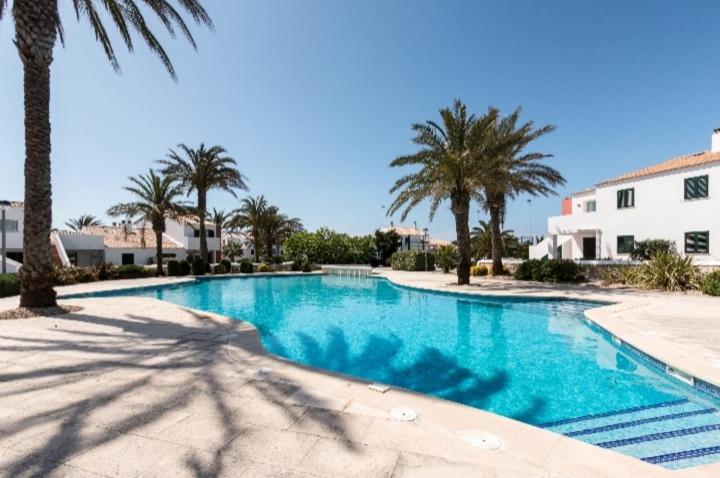 a swimming pool with palm trees and a building at Tranquilo apartamento. Piscina, playa y relax. in Sa Caleta